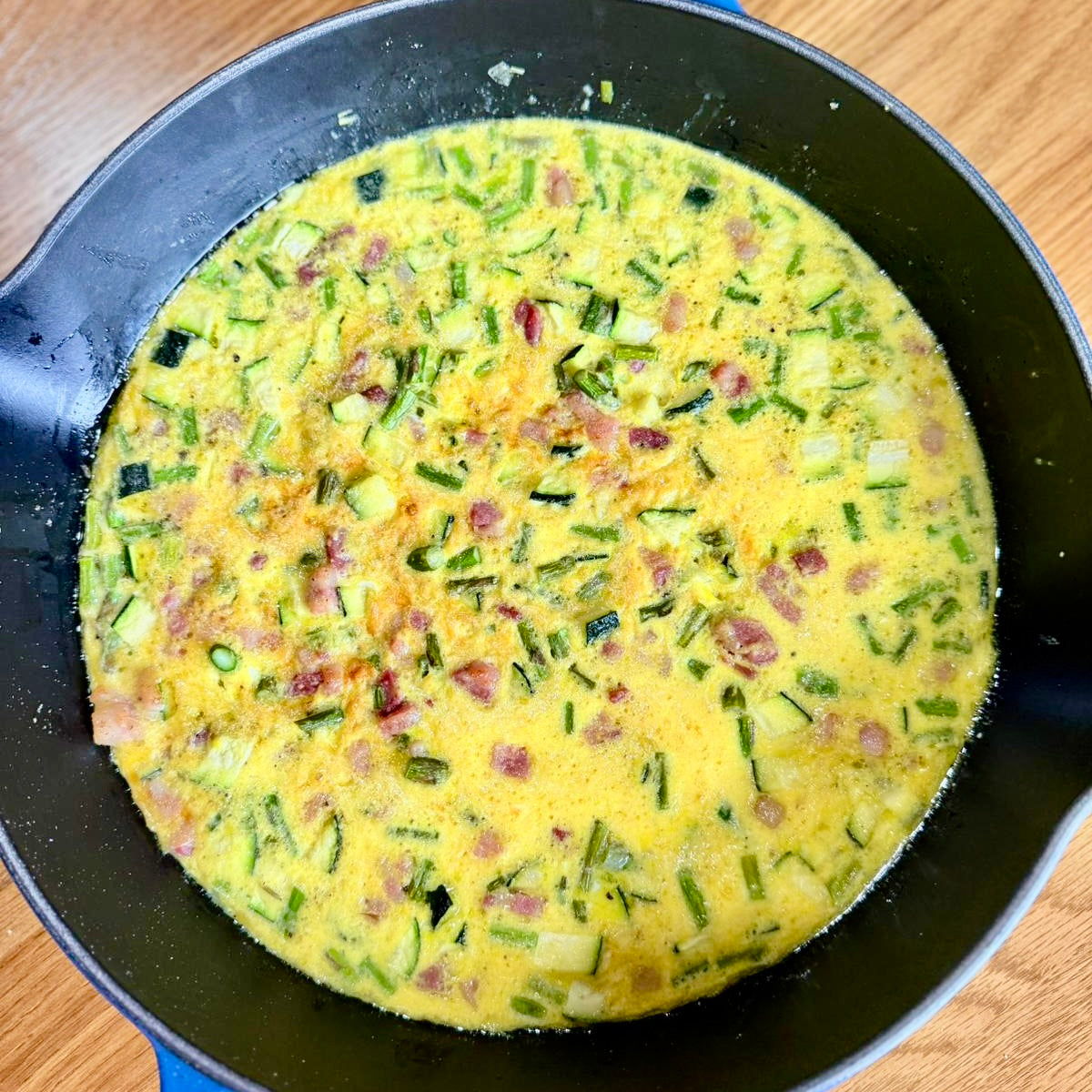 Overhead view of skillet with a frittata made of Parmigiano Reggiano, asparagus, pancetta, and zucchini
