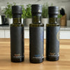 Three bottles of olive oil with black labels on a light surface.